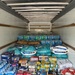 The interior of a large freight trailer is packed floor-to-ceiling with donated or relief food and water supplies. Items include bottled water, rice, pasta, canned goods, oatmeal, and other non-perishable staples, suggesting a disaster relief or food bank distribution effort. The trailer appears nearly full, indicating a large-scale humanitarian supply operation.