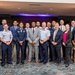 A formal group photograph of approximately 22 individuals posed together in what appears to be a hotel ballroom or conference venue. The group includes a mix of U.S. Air Force military personnel in uniform and civilians in business attire. The composition suggests an official event, ceremony, or professional gathering.