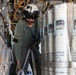 A military aircrew member wearing a flight helmet and olive drab flight suit is working inside what appears to be a maritime patrol or anti-submarine warfare aircraft. The individual is surrounded by rows of cylindrical sonobuoys secured with straps, identifiable by visible markings including 'SSQ-53H' and 'DIFAR' designations. The person appears to be handling or inspecting equipment within the aircraft's sonobuoy storage and launch bay.
