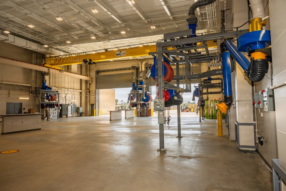 A large, modern industrial maintenance or vehicle service facility with a spacious, clean concrete floor. The facility is equipped with overhead crane systems, exhaust extraction arms, utility reels, and electrical panels mounted on ceiling-level pipe networks. The space appears newly constructed or recently renovated and is currently unoccupied.
