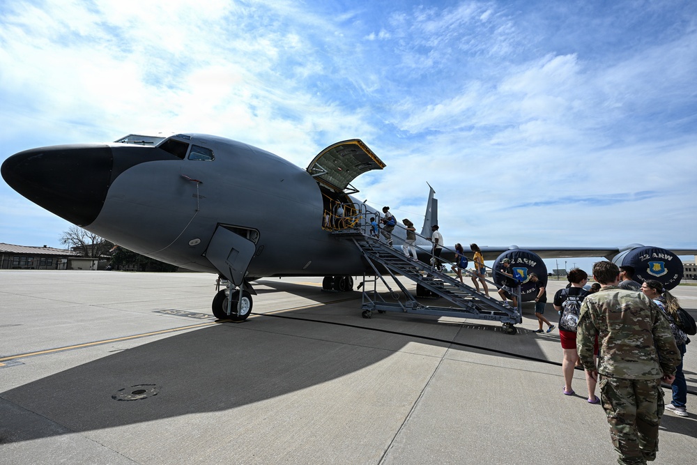 A military aircraft, appearing to be a KC-135 Stratotanker, is parked on a flight line tarmac with a mobile staircase positioned at its forward entry door. Civilians and military personnel are boarding or touring the aircraft, suggesting an open house, air show, or base familiarization event. Unit insignia visible on equipment indicates association with the 22nd Air Refueling Wing (22 ARW).