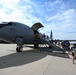 A military aircraft, appearing to be a KC-135 Stratotanker, is parked on a flight line tarmac with a mobile staircase positioned at its forward entry door. Civilians and military personnel are boarding or touring the aircraft, suggesting an open house, air show, or base familiarization event. Unit insignia visible on equipment indicates association with the 22nd Air Refueling Wing (22 ARW).