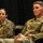 Lt. Col. Hughes and Lt. Col. Pitts promotion ceremony to colonel Two U.S. Army soldiers in Operational Camouflage Pattern (OCP) uniforms are seated side by side against a dark backdrop, appearing to be attending or participating in a formal military event or briefing. The soldier on the right has a visible name tape reading 'PITTS' and 'U.S. ARMY' tape, along with a gold oak leaf cluster rank insignia indicating the rank of Lieutenant Colonel. Both soldiers wear the same unit patch on their left shoulders, identifiable as the 218th Maneuver Enhancement Brigade (South Carolina National Guard palmetto tree patch).