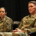 Two U.S. Army soldiers in Operational Camouflage Pattern (OCP) uniforms are seated side by side against a dark backdrop, appearing to be attending or participating in a formal military event or briefing. The soldier on the right has a visible name tape reading 'PITTS' and 'U.S. ARMY' tape, along with a gold oak leaf cluster rank insignia indicating the rank of Lieutenant Colonel. Both soldiers wear the same unit patch on their left shoulders, identifiable as the 218th Maneuver Enhancement Brigade (South Carolina National Guard palmetto tree patch).