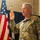 Lt. Col. Hughes and Lt. Col. Pitts promotion ceremony to colonel A U.S. Army soldier in OCP (Operational Camouflage Pattern) uniform is raising his right hand, appearing to take an oath or pledge. An American flag and what appears to be a state flag are visible in the background. The setting appears to be an indoor military ceremony in a brick-walled facility.