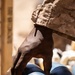 A person wearing desert digital camouflage uniform is handling blue-painted practice mortar rounds stored in a wooden crate. The rounds are visibly marked with 'WARNING' and 'PRACTICE' text, indicating these are inert training munitions. The close-up photograph captures the handling of what appear to be M929/M930-type 60mm or 81mm practice mortar rounds.