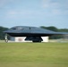 A B-2 Spirit stealth bomber is captured during a ground roll on a runway, appearing to be in the process of taking off or landing. The aircraft is painted matte black and bears visible markings including 'Spirit of Alaska' and the tail code 'WM' along with the serial number '20040'. Motion blur on the background indicates the aircraft is moving at speed.