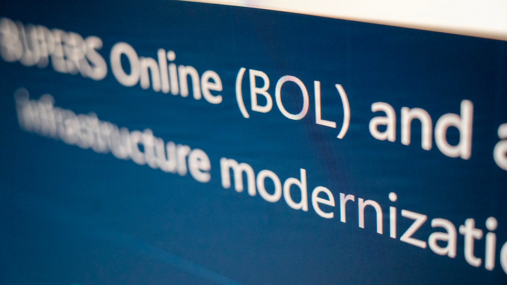 The image shows a close-up photograph of a digital screen displaying white text on a dark blue background. The visible text references 'Online (BOL) and' on the first line, followed by 'Infrastructure modernization' on subsequent lines. The text appears to be part of a presentation slide or webpage, partially cropped at the edges.
