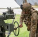 A U.S. Army soldier in full combat gear is operating or adjusting what appears to be an artillery piece, likely an M777 howitzer or similar field artillery system. The soldier is wearing Operational Camouflage Pattern (OCP) uniform with a unit patch visible on the left shoulder, a combat helmet with night vision mount, and tactical vest. The activity appears to be taking place at an outdoor training or operational field site.
