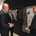 Three men in business attire are engaged in conversation at what appears to be a museum or memorial exhibition focused on '9/11 Response.' A display case containing artifacts, including what appears to be structural debris, is visible beside them. The exhibit wall features text about the United States Army Corps of Engineers' role in the September 11, 2001 terrorist attack response.