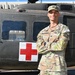 A U.S. Army Captain named McDaniels stands in front of a military medical (MEDEVAC) helicopter, identifiable by the prominent Red Cross marking on its fuselage. He is wearing OCP (Operational Camouflage Pattern) uniform with Captain rank insignia and a 'Competitor 22' armband, suggesting participation in a military competition. The photo appears to be an official or promotional portrait taken outdoors in clear daylight.