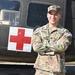 A U.S. Army Captain named Alicea stands confidently with arms crossed in front of a military medevac helicopter marked with a Red Cross symbol. He is wearing the Operational Camouflage Pattern (OCP) uniform with Captain rank insignia (two silver bars) visible on his chest. The setting appears to be an outdoor military display or installation.