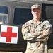 A U.S. Army Staff Sergeant named Tweeddale stands at attention with arms crossed in front of a military medevac helicopter marked with a Red Cross symbol. He is wearing Operational Camouflage Pattern (OCP) uniform with visible rank insignia, name tape, U.S. Army tape, and a competition number patch on his right sleeve. The image appears to be an official or semi-official military portrait photograph.