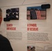 A museum exhibit display showing two panels related to the September 11, 2001 Pentagon attack. The panels are titled 'Search and Rescue' (+3 Hours) and 'A Symbol of Resolve' (+32 Hours), featuring historical photographs and descriptive text. A man with gray hair, viewed from behind, is reading the exhibit wall.