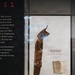 A museum display case contains two artifacts related to the September 11, 2001 terrorist attacks: a twisted, heavily corroded structural steel beam from the World Trade Center and a limestone fragment from the Pentagon. The exhibit label reads 'LEFT TO RIGHT: Structural steel from the World Trade Center / Limestone fragment from the Pentagon.' Partial wall text on the left references the 2001 terrorist attacks and the United States Army Corps of Engineers' response role.