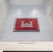 The image shows a museum or exhibition space featuring a framed red flag with a white castle emblem — the insignia of the U.S. Army Corps of Engineers (USACE) — mounted high on a light-colored wall. The flag appears to be signed by multiple individuals and is displayed as an artifact. Surrounding wall text references 'USACE AT GROUND ZERO' and includes a quote attributed to SGT 1ST CLASS JEREMY ZEMAITIS, 249TH ENGINEER BATTALION.