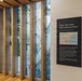 This image shows an interior exhibit space, likely from the 9/11 Memorial Museum in New York City. The display features interpretive panels, a large aerial photograph of lower Manhattan visible through vertical wooden slats, and informational text about the September 11, 2001 terrorist attacks. The exhibit includes a prominent quote from Joe Vietri, New York District, reading 'Crisp, clear skies. Not a cloud up there.'