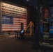 A museum exhibit dedicated to the United States Army's involvement in World War II. The centerpiece is a large illuminated display featuring an American flag made of soldier figurines, accompanied by statistics about soldiers who served, died, or were wounded. The exhibit includes artifacts, informational panels, and display cases related to the Army in Europe.