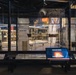 This image shows a museum exhibit dedicated to 'Nuclear Power,' featuring artifacts displayed behind glass panels including what appears to be a historic aircraft or seaplane and rocket/missile models. Interactive digital touchscreen displays are positioned in the foreground, inviting visitors to engage with the content. The exhibit is part of a larger museum floor that also references 'Space' in adjacent sections.