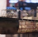 The image shows a detailed scale model of a U.S. Army Corps of Engineers vessel displayed in what appears to be a museum or exhibition setting. The model features a dark hull with white superstructure, crane equipment, and intricate deck details. A glass display case reflection reveals additional ship models in the background.