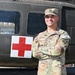 A U.S. Army soldier identified by name tape as 'Morgan' stands with arms crossed in front of a military medical helicopter marked with a Red Cross symbol. The soldier wears OCP (Operational Camouflage Pattern) uniform with Staff Sergeant rank insignia on the cap and a '2nd Infantry Division' patch on the left shoulder. A 'COMPETITOR 20' tab is visible on the right sleeve, suggesting participation in a military competition.