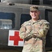 A U.S. Army Staff Sergeant named Lopez stands with arms crossed in front of a military medical helicopter marked with a Red Cross symbol. He is wearing OCP (Operational Camouflage Pattern) uniform with visible rank insignia and name tape. The image appears to be an official or semi-official portrait-style photograph taken outdoors.