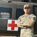 A U.S. Army soldier named Peña, wearing Operational Camouflage Pattern (OCP) uniform, stands with arms crossed in front of a military medical helicopter marked with a Red Cross symbol. The soldier is wearing a competitor bib numbered '26', suggesting participation in a military competition. The image appears to be an official or semi-official portrait-style photograph.