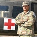 A U.S. Army Staff Sergeant named Willis stands with arms crossed in front of a military medical helicopter marked with a Red Cross symbol. He is wearing OCP (Operational Camouflage Pattern) uniform with visible rank insignia, name tape, U.S. Army tape, and a unit patch on his left shoulder. The image appears to be an official or promotional military portrait.