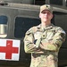 A U.S. Army soldier named Huber stands with arms crossed in front of a military medical helicopter marked with a red cross. He is wearing Operational Camouflage Pattern (OCP) uniform with visible rank insignia, name tape, and unit patches. The image appears to be an official or promotional military portrait taken outdoors in good lighting.
