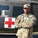 A U.S. Army soldier named Brown stands at attention with arms crossed in front of a military medical helicopter marked with a Red Cross symbol. The soldier is wearing Operational Camouflage Pattern (OCP) uniform with 'US ARMY' and 'BROWN' name tapes visible, along with unit patches. The setting appears to be an outdoor military installation or display area.