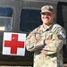 A U.S. Army Sergeant named Rodriguez stands at ease with arms crossed in front of a military medical vehicle marked with a Red Cross symbol. He is wearing Operational Camouflage Pattern (OCP) uniform with visible rank insignia, name tape, U.S. Army tape, a unit patch, and a 'Competitor 2' label. The image appears to be an official or promotional military photograph.