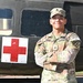 A U.S. Army Sergeant named Velez stands with arms crossed in front of a military medical helicopter marked with a Red Cross symbol. The soldier is wearing Operational Camouflage Pattern (OCP) uniform with visible rank insignia, name tape, U.S. Army tape, and a unit patch. The image appears to be an official or promotional military photograph taken outdoors in daylight.