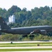 A U.S. Air Force KC-135 Stratotanker aerial refueling aircraft is captured during takeoff or landing at a military airfield. The aircraft bears ANG (Air National Guard) markings on the tail with serial number 60099 and a Pennsylvania ANG designation. The gray military aircraft is photographed against a backdrop of dense green trees.
