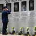 A uniformed U.S. Air Force service member renders a salute at a memorial wall honoring fallen airmen, primarily from the 58th Fighter Squadron who died on 25 June 1996. The granite memorial wall features engraved portraits and biographical inscriptions of the deceased, with military boots and yellow flowers placed at its base as tributes. The header text reads 'OUR NOMADS' and the setting appears to be an outdoor memorial ceremony.