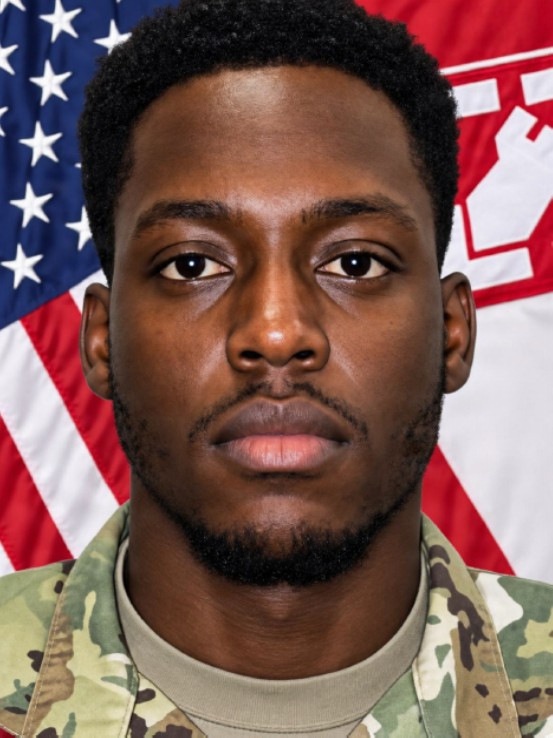 A formal military portrait photograph of a young male service member wearing US Army OCP (Operational Camouflage Pattern) uniform. He is posed in front of two flags: the United States flag on the left and what appears to be a US Army Corps of Engineers flag on the right. The image is a standard official military headshot.