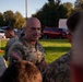 A U.S. Army Colonel named Bithorn, identifiable by the eagle insignia on his uniform, is engaged in conversation with a group of soldiers in an outdoor setting. The scene appears to take place during early morning or late afternoon based on the warm, low-angle lighting. Multiple personnel in OCP (Operational Camouflage Pattern) uniforms are gathered in what appears to be a briefing or informal discussion.