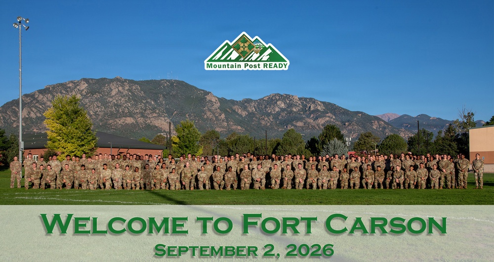 A large group photo of military personnel in camouflage uniforms assembled on a green athletic field at Fort Carson, Colorado. The image is formatted as a welcome graphic dated September 2, 2026, featuring the 'Mountain Post READY' logo. The Rocky Mountains are prominently visible in the background under a clear blue sky.