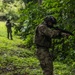 Two soldiers in multicam camouflage uniforms are conducting a patrol or training exercise along a jungle trail. The foreground soldier is in an aiming stance with a rifle, while a second soldier is visible further down the path. A small flag patch is visible on the foreground soldier's helmet, identifiable as the Panamanian flag.