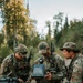Three U.S. Army soldiers in MultiCam/OCP camouflage uniforms are gathered around the bed of a pickup truck in a forested outdoor environment. They are operating Parrot-branded drone equipment, including a rugged tablet controller and a carrying case. The setting appears to be a field training exercise or operational deployment.