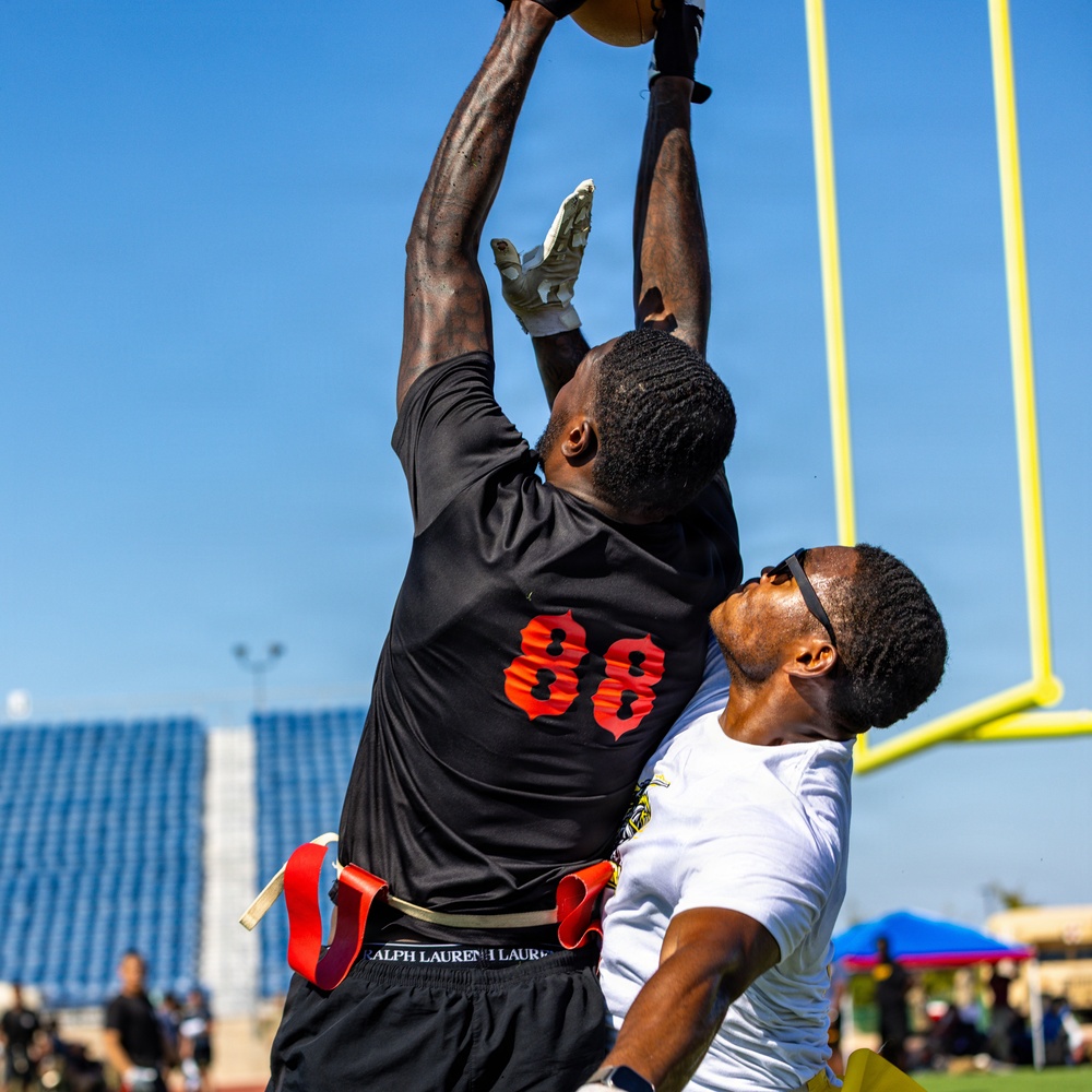 A flag football game is in progress near the end zone, with player number 88 in a black jersey leaping to catch or contest a football at its highest point. A defender in a white jersey attempts to challenge the play from behind. The yellow goal post is prominently visible in the background, confirming the near-end-zone location.