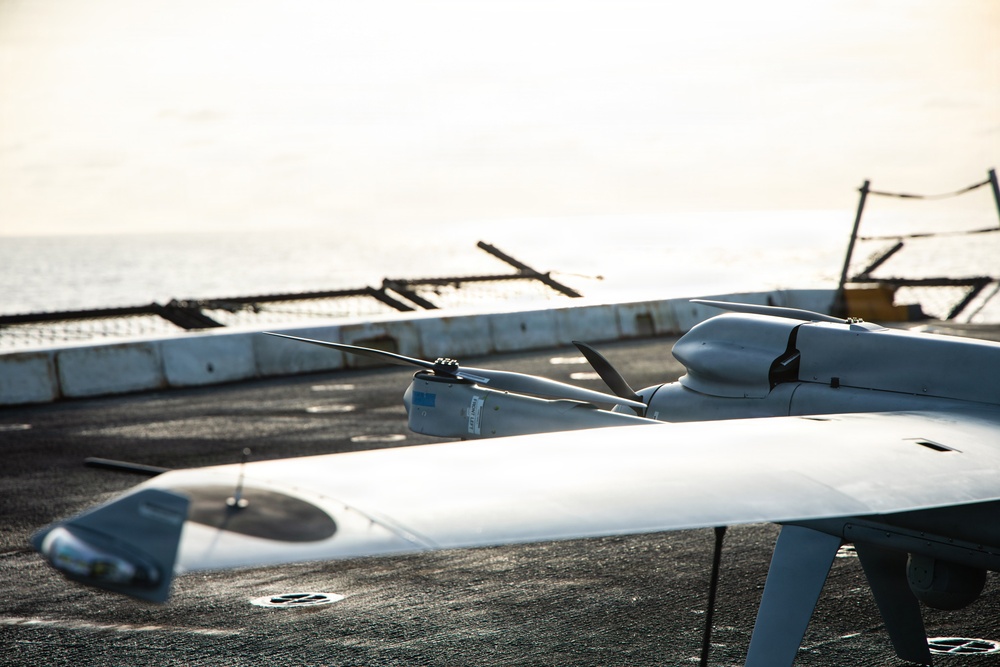 The image shows one or more unmanned aerial vehicles (UAVs/drones) positioned on what appears to be the deck of a naval vessel at sea. The UAVs have a fixed-wing design with a pusher propeller configuration and appear to be military or surveillance-grade systems. The ocean is visible in the background, confirming a maritime operational environment.