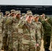 A formal military ceremony showing U.S. Army soldiers and what appear to be Japanese Self-Defense Force personnel rendering salutes simultaneously. The soldiers are standing in organized rows inside what appears to be a gymnasium or indoor facility. Visible name tapes and rank insignia identify several U.S. Army personnel, suggesting a joint military event.