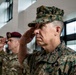 Multiple military personnel in various uniforms are rendering a salute during what appears to be a formal ceremony or official event. The foreground figure wears United States Marine Corps MARPAT digital camouflage with three-star rank insignia (Lieutenant General). Behind him are Army personnel, including one wearing a maroon beret associated with airborne units.