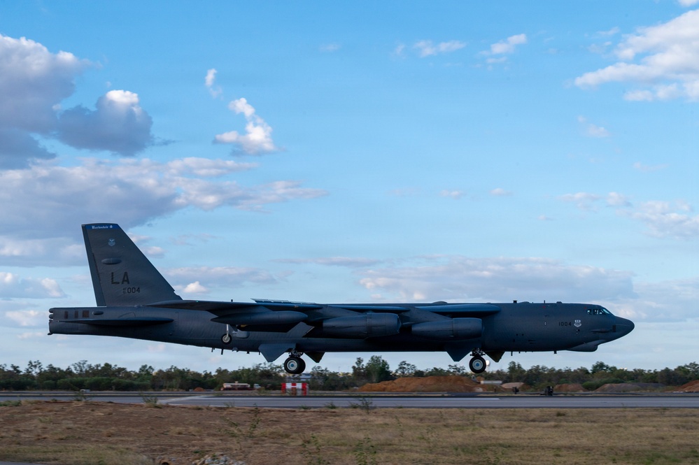 A U.S. Air Force B-52 Stratofortress strategic bomber is captured during takeoff or landing on a runway. The aircraft bears the tail code 'LA' and serial number ending in '004', indicating assignment to Barksdale Air Force Base, Louisiana. The setting appears to be an overseas or forward operating location based on the surrounding terrain and vegetation.