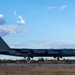 A U.S. Air Force B-52 Stratofortress strategic bomber is captured during takeoff or landing on a runway. The aircraft bears the tail code 'LA' and serial number ending in '004', indicating assignment to Barksdale Air Force Base, Louisiana. The setting appears to be an overseas or forward operating location based on the surrounding terrain and vegetation.