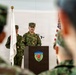 A military officer in Japanese Ground Self-Defense Force camouflage uniform is delivering a speech at a podium during a formal ceremony. The podium bears a shield-shaped insignia that reads 'Ground Component Command.' Both Japanese and American flags are visible in the background, indicating a joint military event.