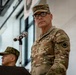 A senior U.S. Army officer wearing three-star general rank insignia stands at a podium with a microphone, appearing to deliver remarks at a formal military ceremony or event. He is dressed in OCP (Operational Camouflage Pattern) uniform with a 'RANGER' tab and U.S. Army tape visible. A second military figure in a different camouflage pattern is visible in the background.