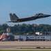 A U.S. Air Force F-15 Eagle fighter jet is captured in a low-altitude takeoff or flyby over what appears to be a joint civilian-military airfield. The aircraft displays tail codes 'ZZ' and '18', indicating it belongs to the 18th Wing based at Kadena Air Base, Japan. A Southwest Airlines Boeing 737 is visible in the background, confirming the shared civilian-military airport setting.