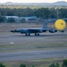 A large military bomber aircraft, identifiable as a B-52 Stratofortress, is landing on a runway with a bright yellow drag parachute deployed behind it to assist in deceleration. The aircraft is on the ground with all landing gear visible, rolling down the tarmac. The setting appears to be a military airfield surrounded by sparse vegetation, low buildings, and hills in the background, consistent with an Australian location.
