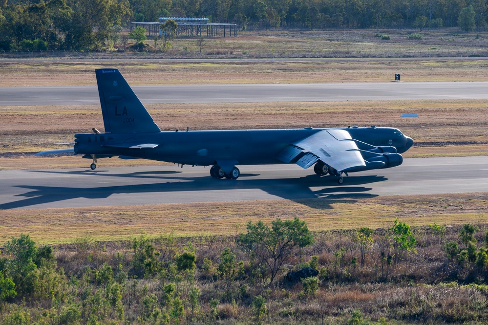A U.S. Air Force B-52 Stratofortress strategic bomber is taxiing on a runway at what appears to be an airfield in a tropical or semi-arid environment. The aircraft bears the 'LA' tail code, indicating assignment to Barksdale Air Force Base, Louisiana, home of the 2nd Bomb Wing. The setting, with dry grass and eucalyptus-type vegetation, suggests this may be RAAF Base Darwin or a similar Australian airfield.